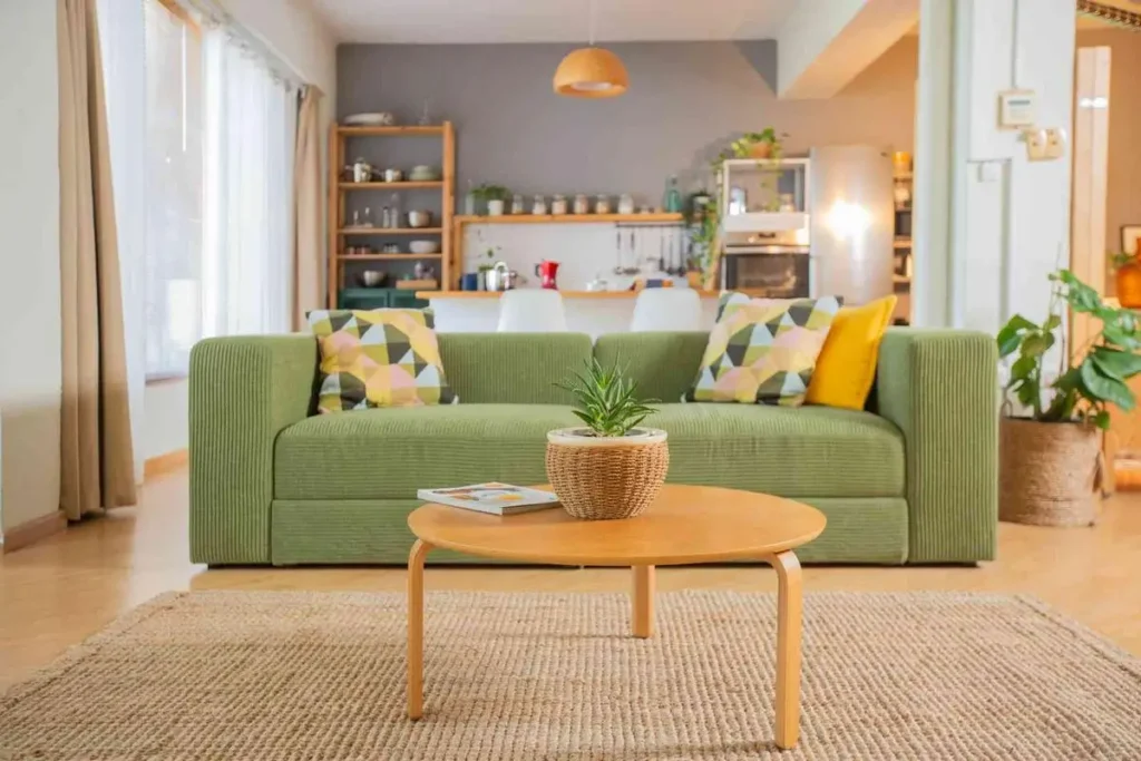 Salón con sofá verde, cojines, mesa redonda de madera y plantas en el Urban Studio
