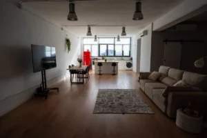 Salón luminoso del Flex Studio con sofá, pantalla y grandes ventanales