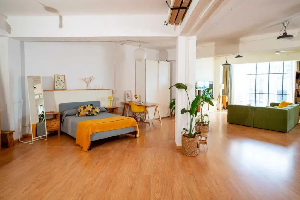 Dormitorio del Urban Studio con cama, espejo de pie y luz natural de ventanal