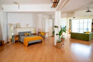 Dormitorio del Urban Studio con cama, espejo de pie y luz natural de ventanal